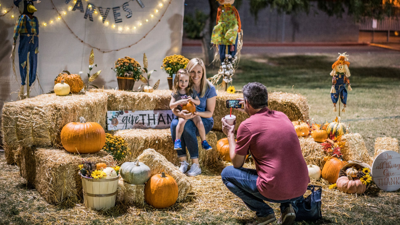 Mother holds a child on hay bales as father takes a photograph