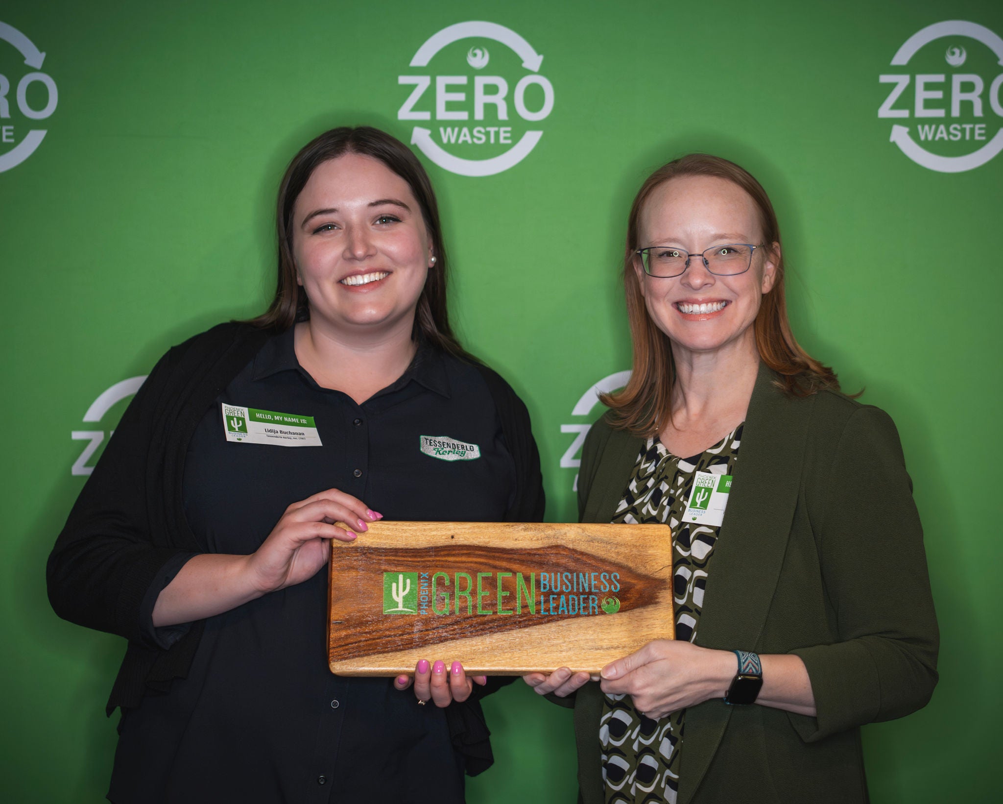 A new Green Business Leader holds his recognition plaque in front of a green backdrop with the Zero Waste logo all over it