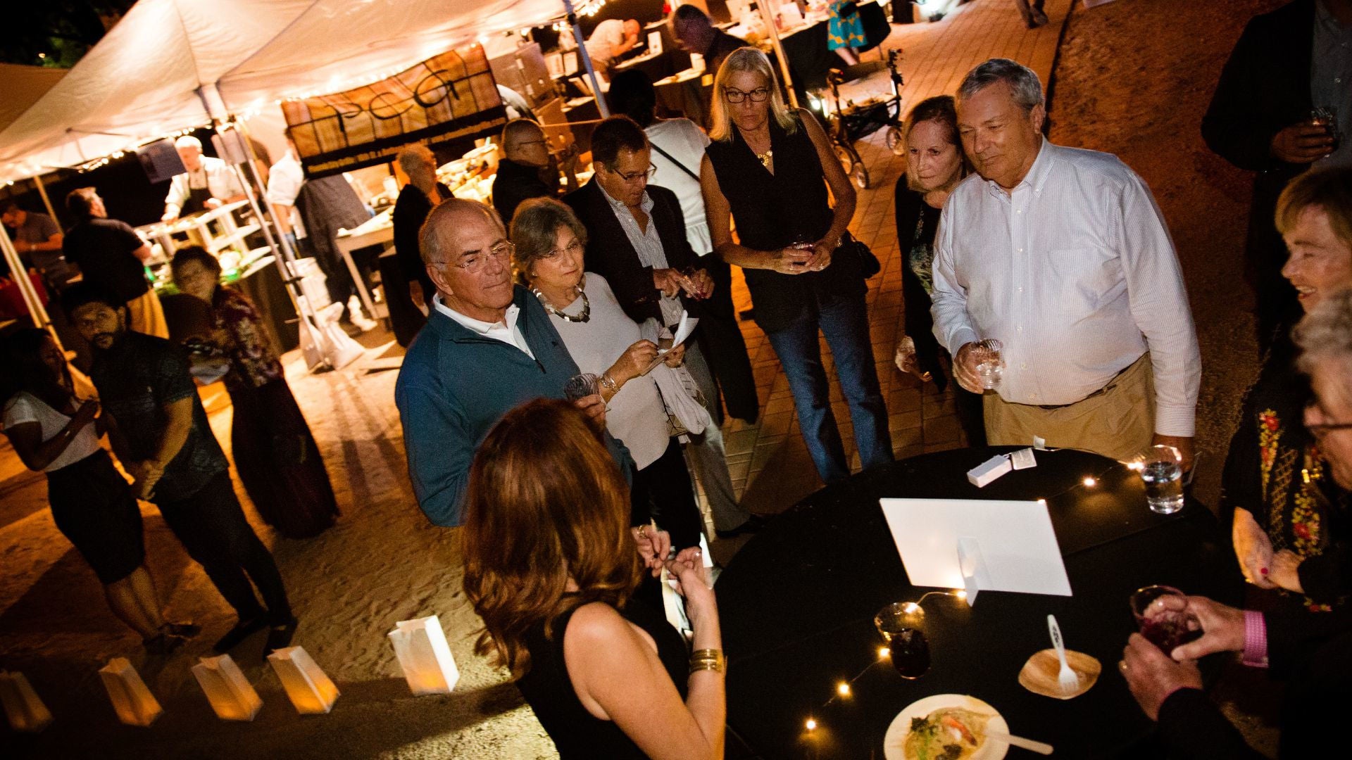 Photo of a gorup of people in formal wear surrounding a candle lit hightop table at a past S'edav Va'aki Museum fundraiser gala. 