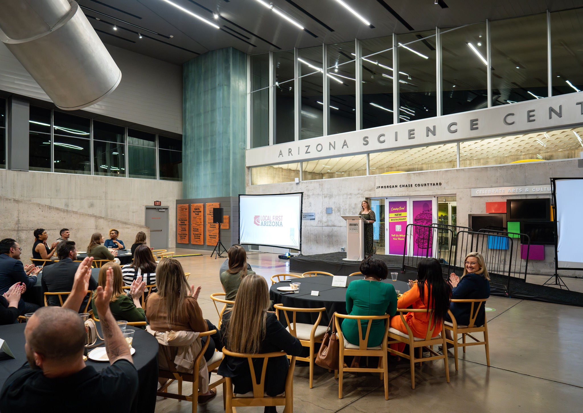 A photo of the crowd seated around tables and listening to speakers t the Arizona Science Center.