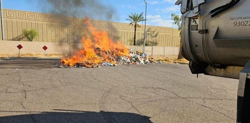 Large orange flames rise from a load of burning trash behind a Phoenix garbage truck.