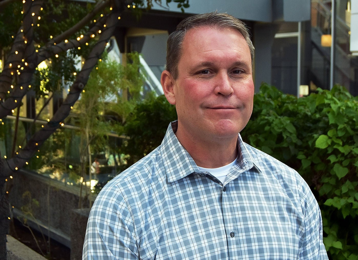 White male with brown hair in a light blue plaid button-down, long-sleeved shirt 