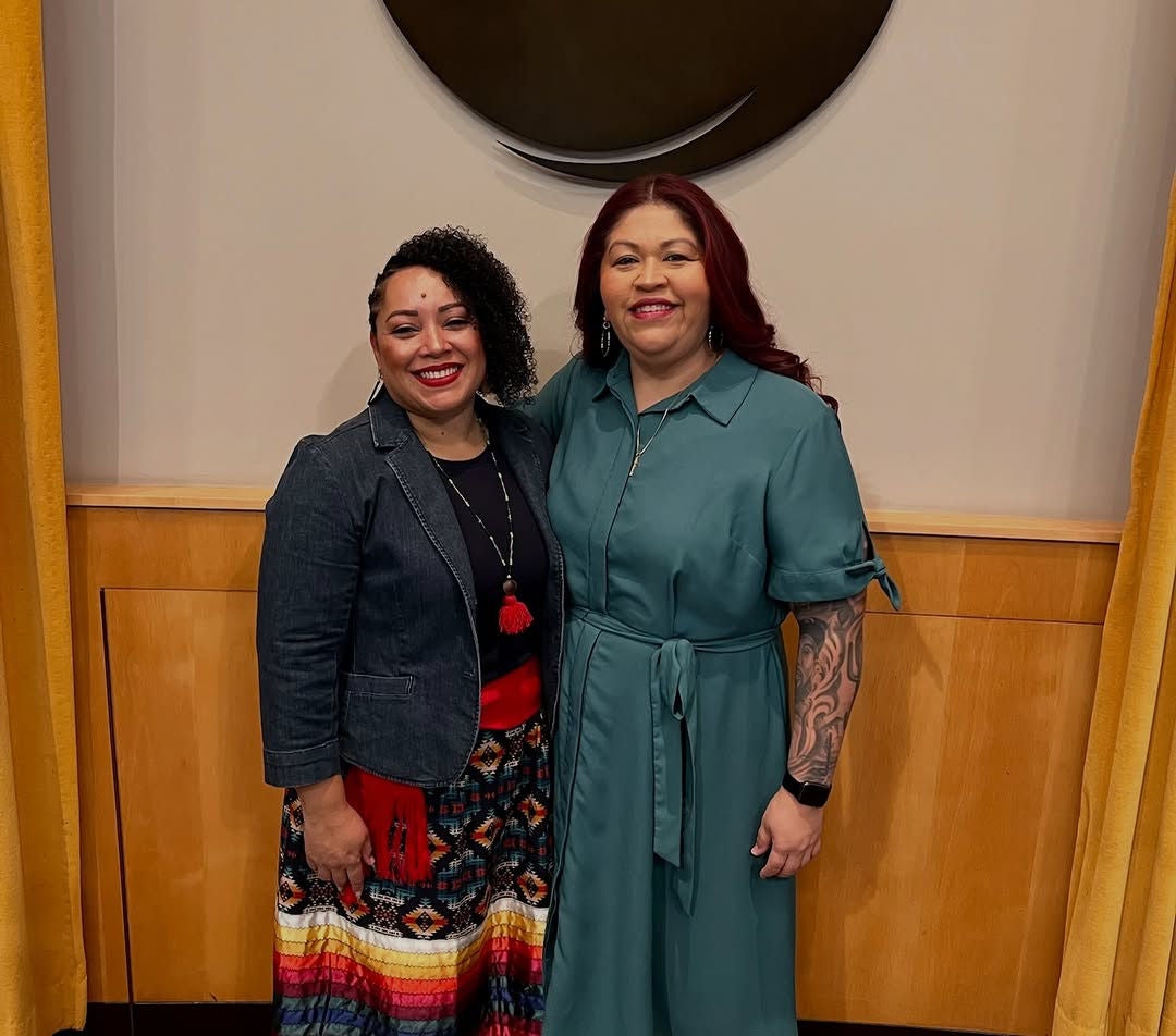 Dr. Enjolie Lafaurie, co-founder of D7's Cihuapactli Collective and newly sworn member of the City of Phoenix Human Services Commission, stands smiling with Councilwoman Anna Hernandez inside City Hall, both dressed for the occasion.