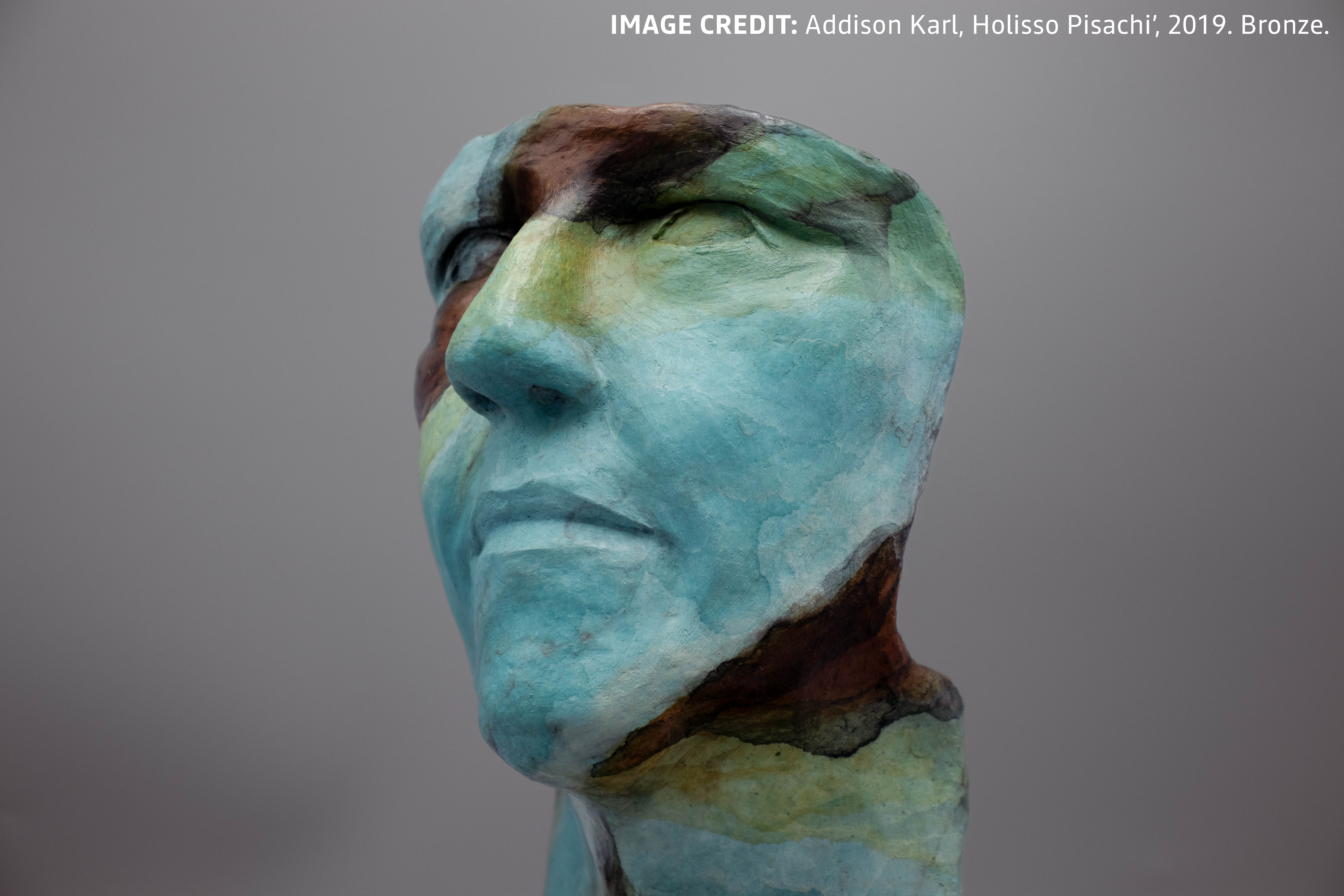 Photo of Holisso Pisachi' by Addison Karl. A bust casted in bronze, oxidized to show various colors including but not limited to teal, green, yellow, and brown. 