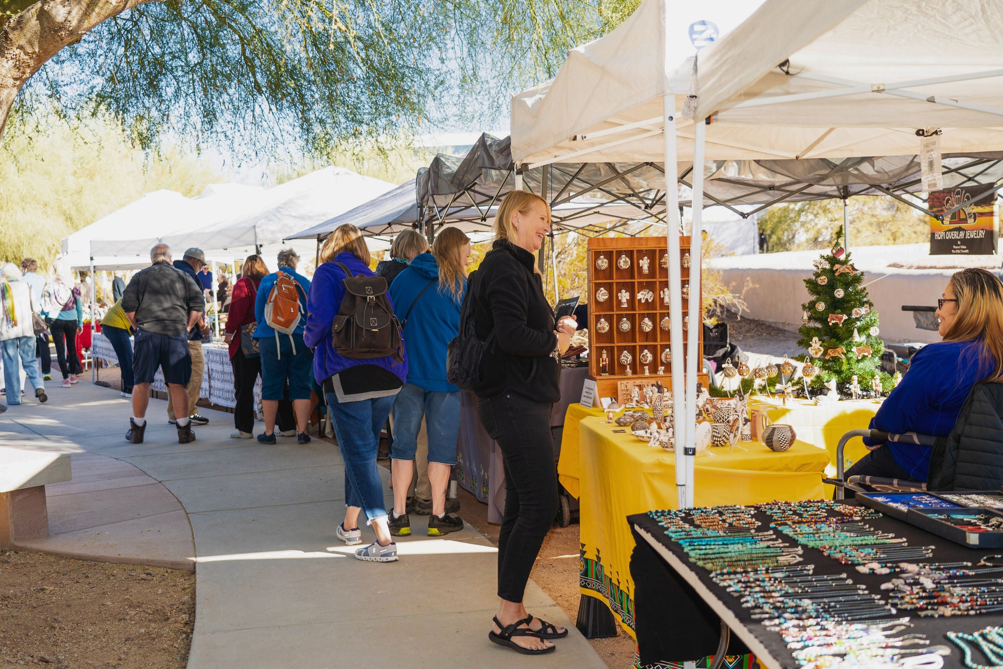 Photo of woman shopping at a vendor's booth with a crowd and other booths in the background.