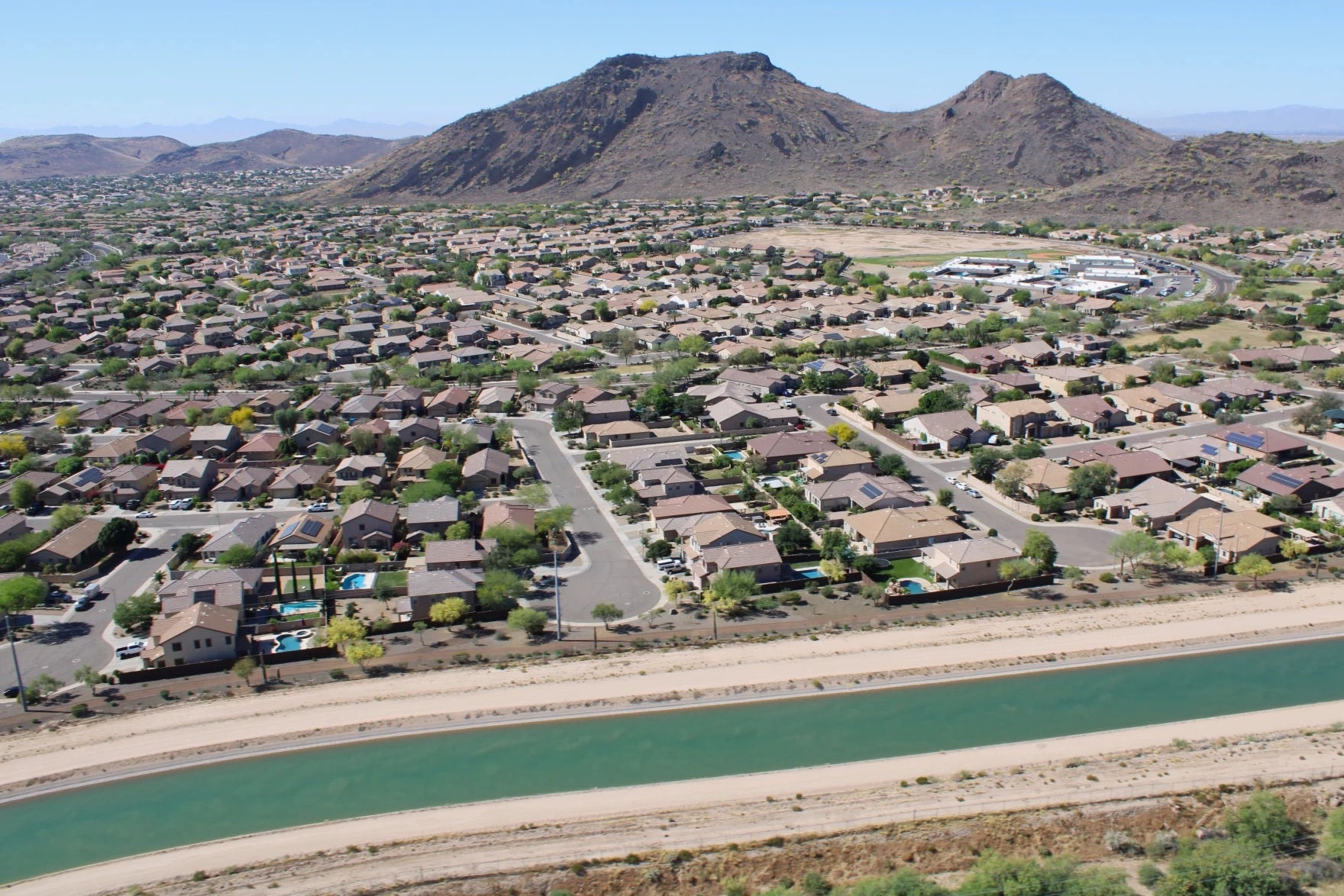 The Central Arizona Project canal carries Colorado River water past a suburban neighborhood in north Phoenix, with desert mountains in the background. The amount of water flowing through the canal could be cut significantly under new federal plans to rein in demand.