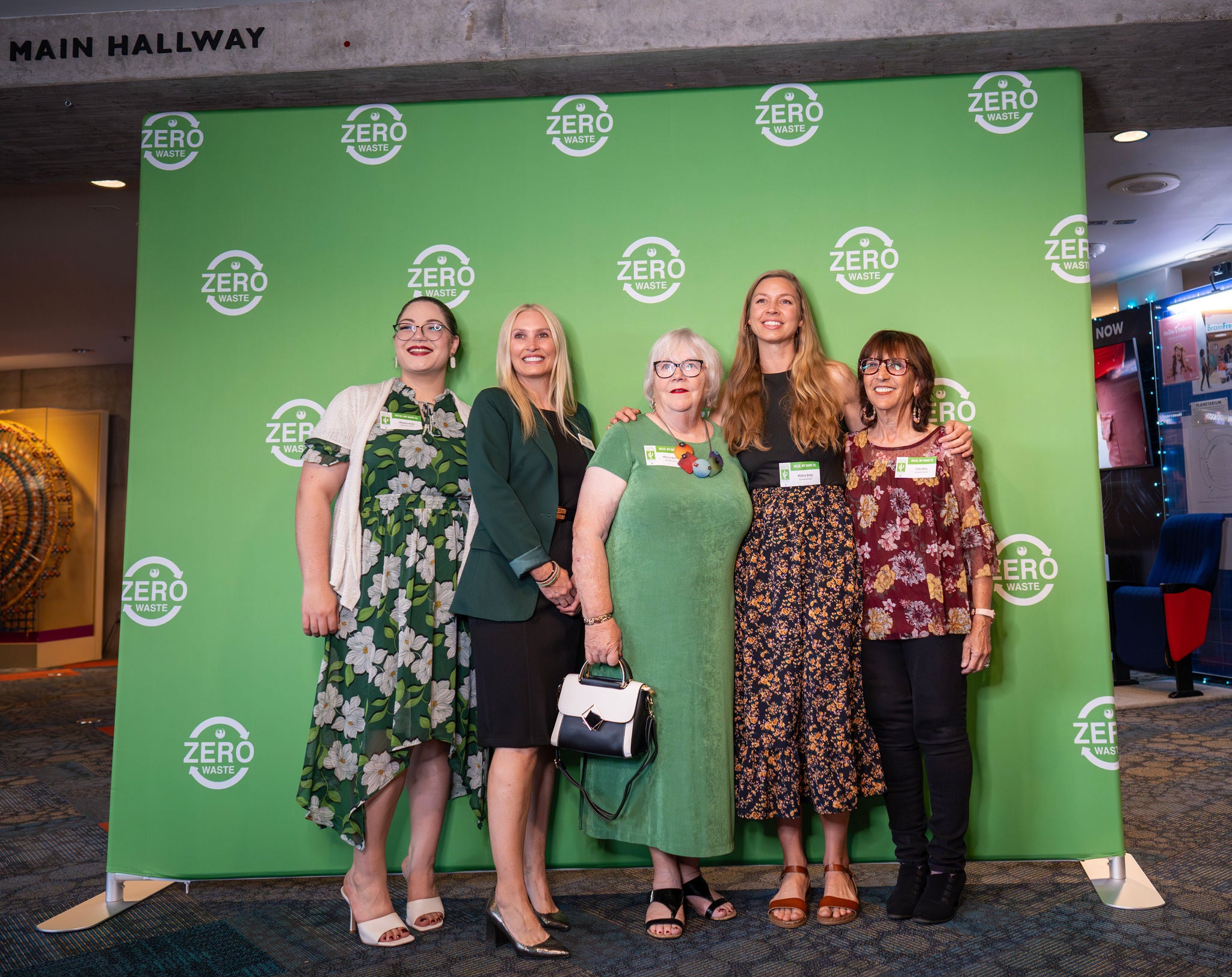 Guests from Keep Phoenix Beautiful stand for a photo opp in front of a green backdrop that is filled with the Zero Waste logo.