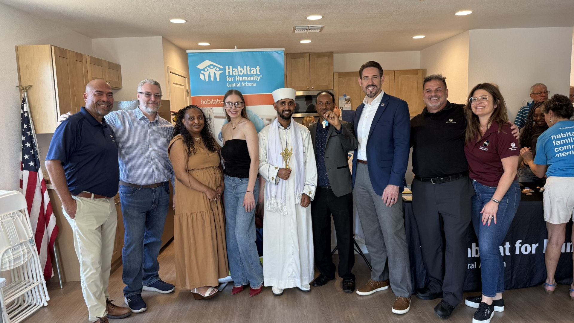 A group of people stand together in front of a Habitat for Humanity banner inside of a newly built home, with one person holding up a set of keys.
