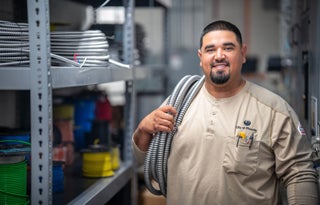Electrician in uniform holding flexible tubing on his right shoulder