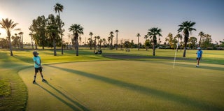 Two individuals play golf at sunset.