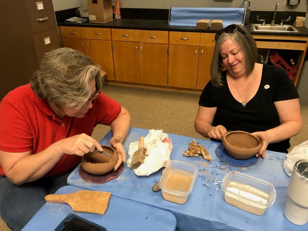 Two women at a table hand sculping clay pottery at a workshop hosting in 2017.