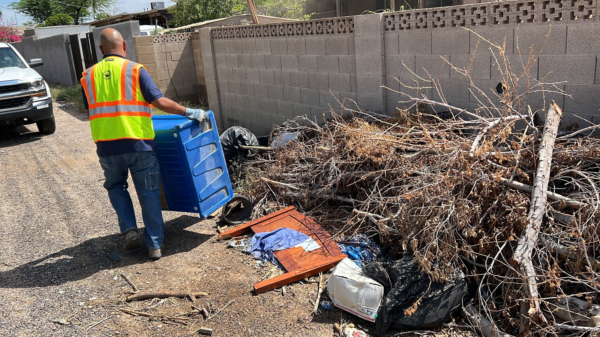 A customer engagement specialist in a neon vest moves a large, blue bin from a pile of trash that was illegally dumped in an alley.