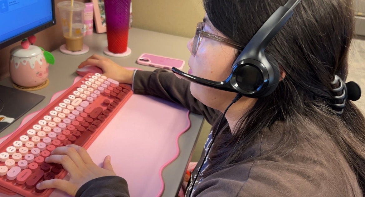 A call center agent with a headset speaks with a customer on the phone while inputting data on the computer/