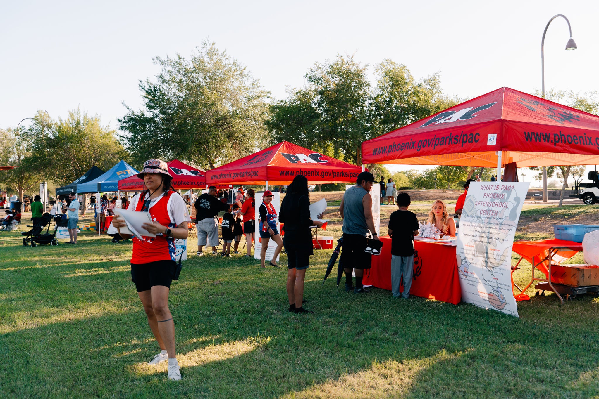 Photo of vendor tents at an event in the park, with people standing at the tents lining up for services.