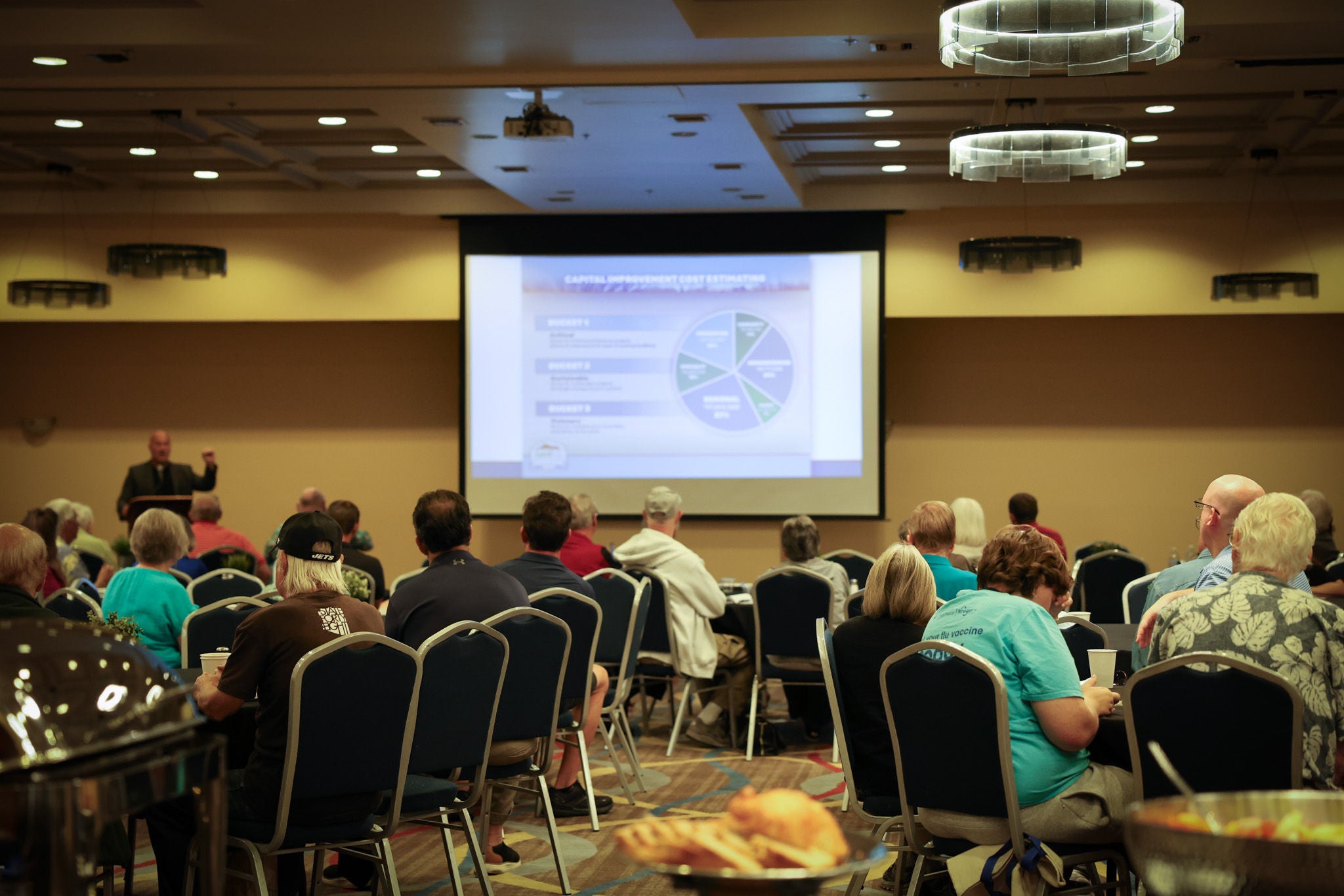 People sitting at tables watching a presentation on a screen.