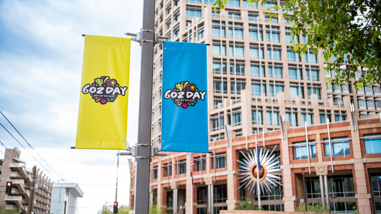 Two banners with colorful 602 Day logo art fixed to a street light pole in front of Phoenix City Hall