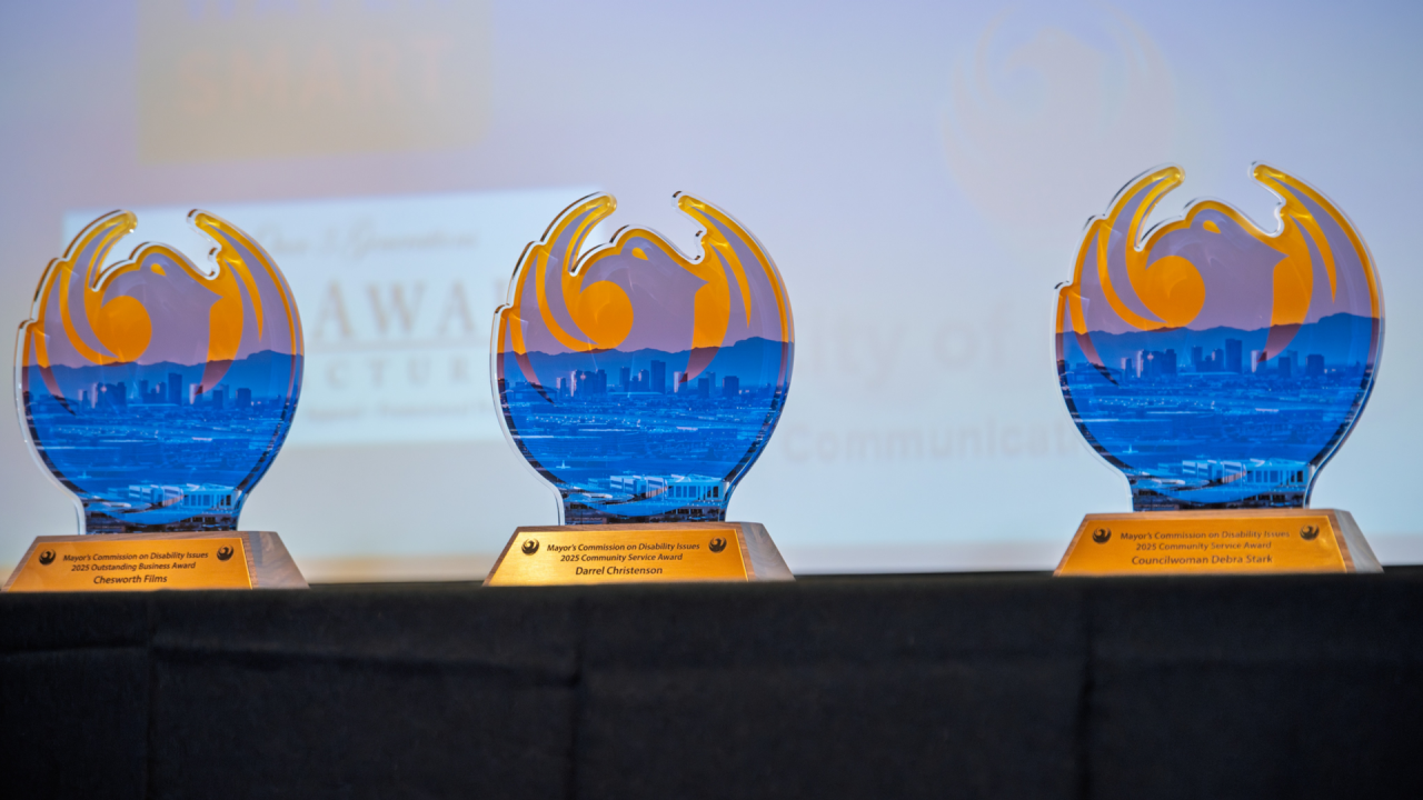 Image of three award statues in the shape of a Phoenix bird with a gold base. They are sitting on a black table with a glowing screen in the background. 