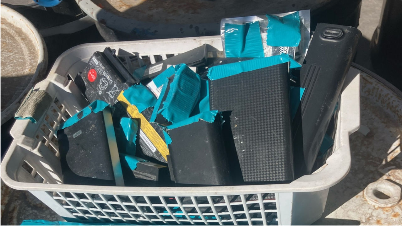 A laundry basket full of old lithium-ion batteries of various shapes and sizes with their ports taped over for safety.