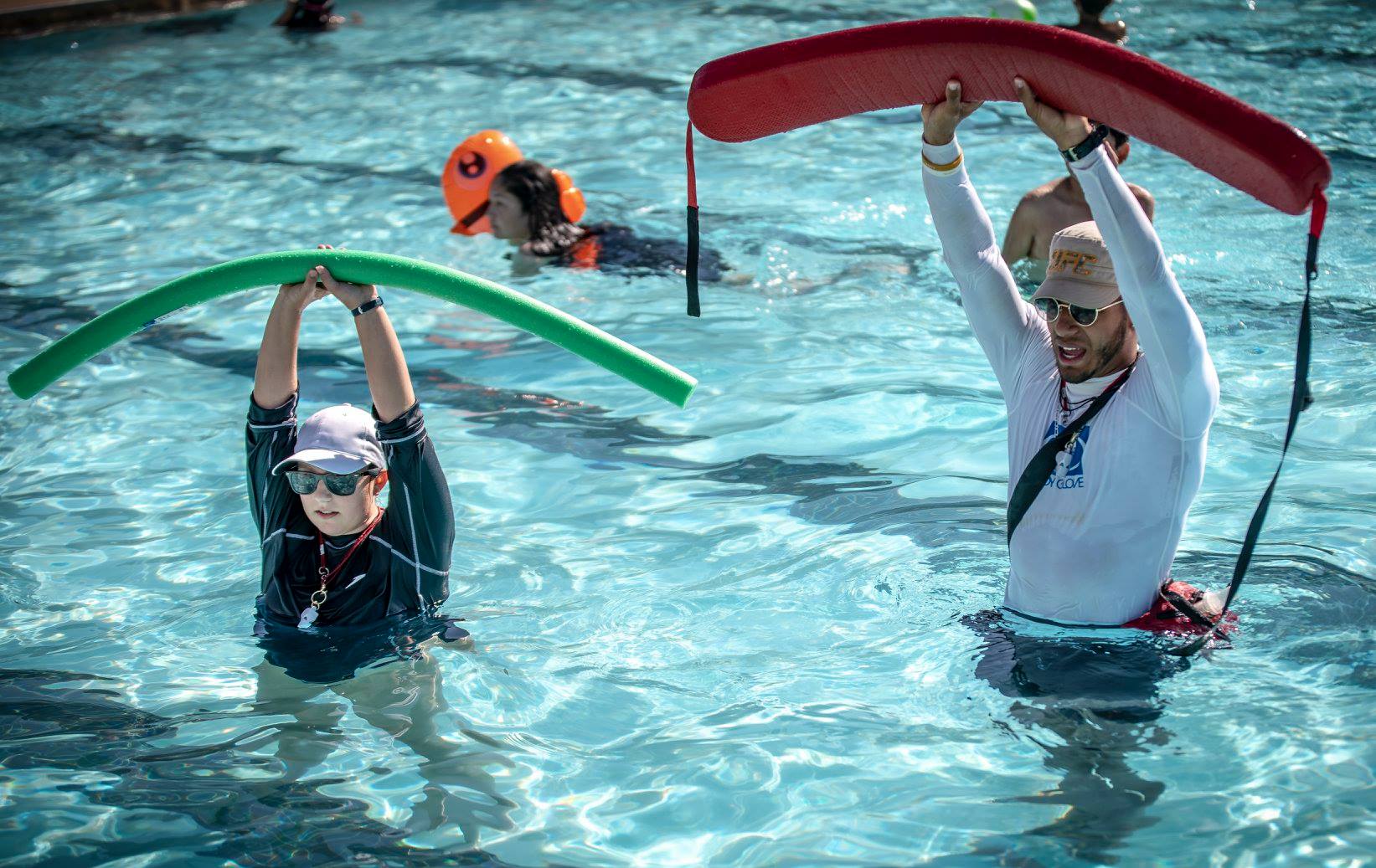 Lifeguard teaching swimmer how to use kickboard