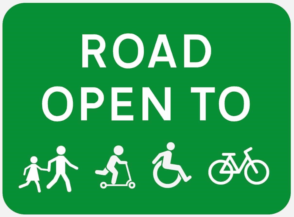 Green traffic sign that reads "ROAD OPEN TO" and depicts icons of people walking, riding scooters, a wheelchair, and a bicycle