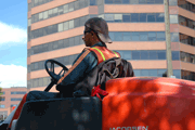 Man riding powered lawnmower, with hi-rise buildings in the background.