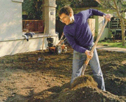 Man in sweatshirt shoveling dirt in yard.