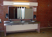 Stainless steel restroom sink with large mirror overhanging.
